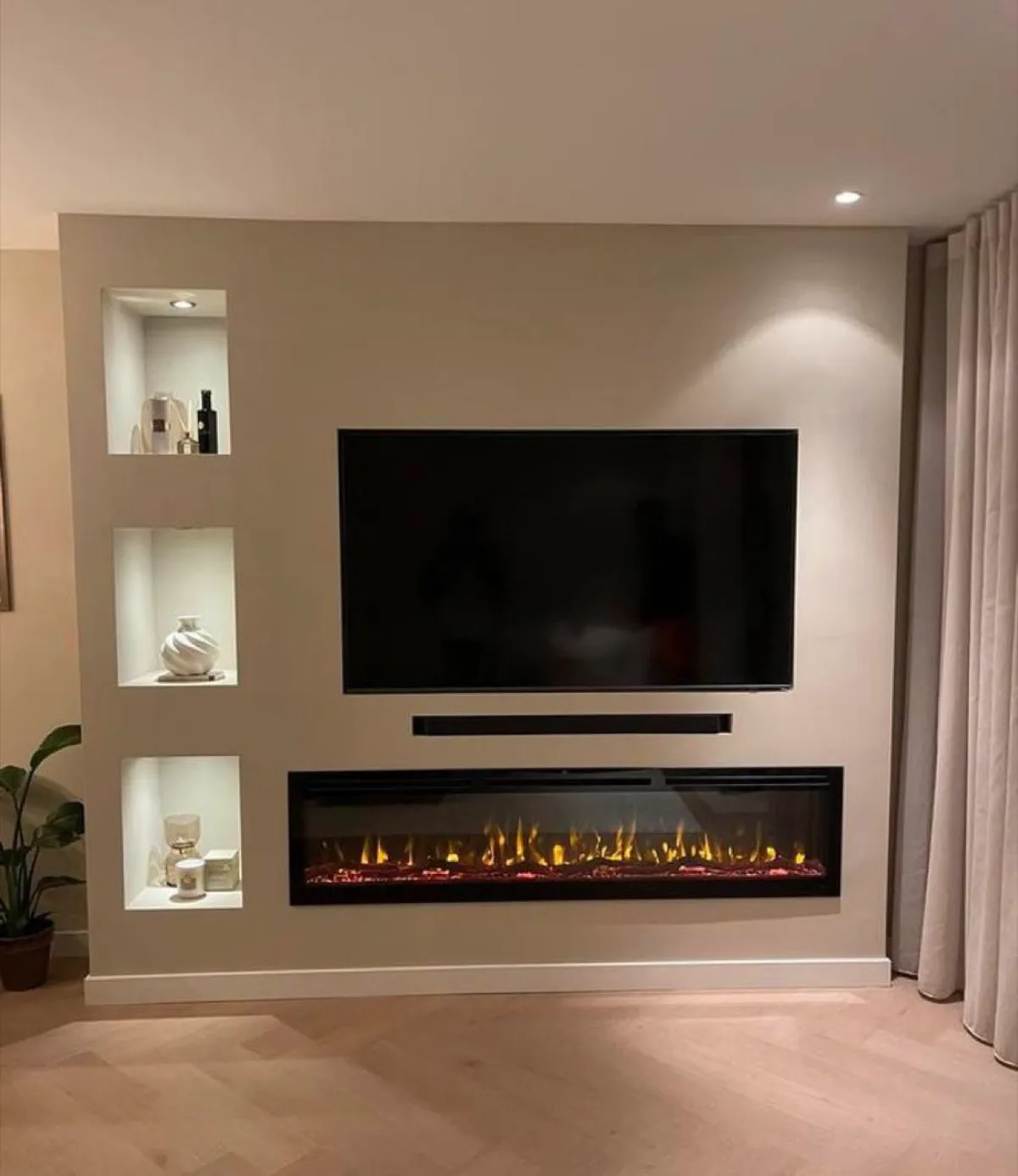 Gerealiseerde Cinewall met warm verlichte nissen, brede sfeerhaard en gordijnen aan weerszijden